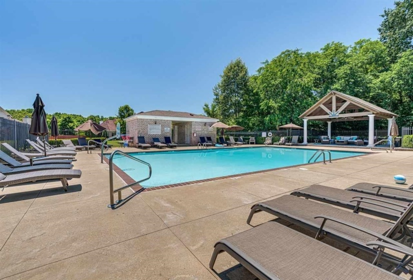 Outdoor pool area featuring a rectangular pool with concrete surround, a brick building, and a shaded pavilion with columns