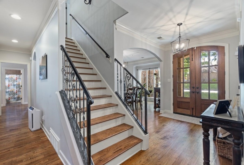 Entryway featuring double wood-paneled doors with glass inserts, a grand staircase with decorative wrought iron balusters, hardwood flooring, an arched doorway, and crown molding