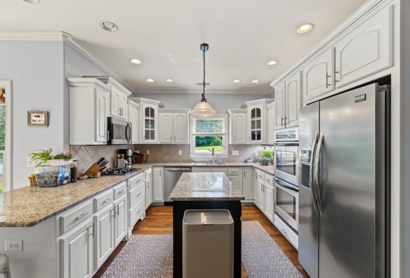 Kitchen featuring white cabinetry, granite countertops, gas cooktop, stainless steel appliances, a central island with a contrasting base, and hardwood flooring