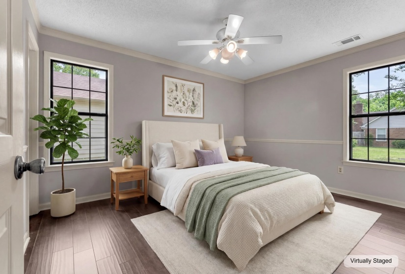 Spacious room featuring wood-finish flooring, two large windows, a ceiling fan with integrated lighting, and crown molding details