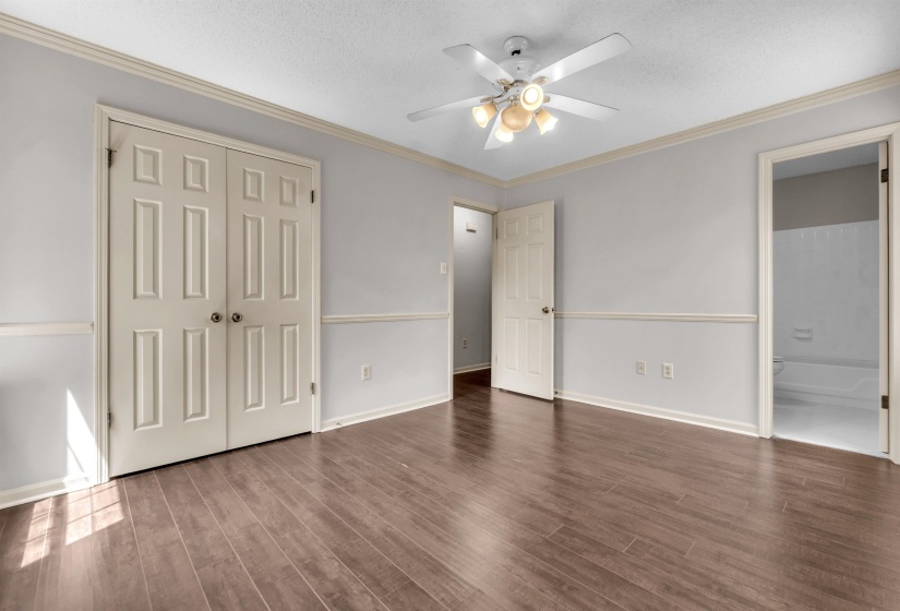 Spacious interior room featuring wood-finish flooring, light gray wall paint with white wainscoting, and white crown molding