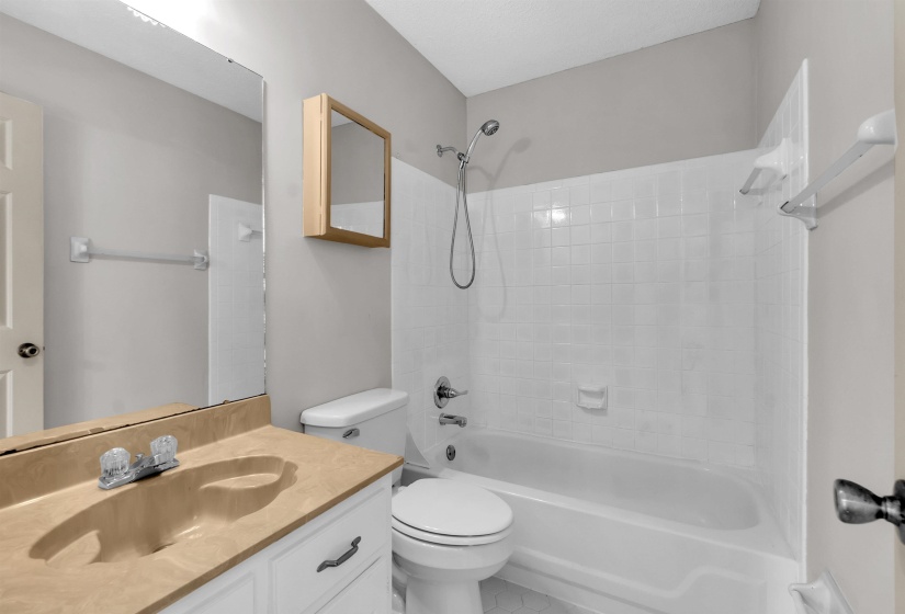 Full bathroom featuring a vanity with a built-in sink and countertop, white cabinetry with dark hardware, an overhead mirror, a built-in medicine cabinet, and a shower/tub combination with a tiled surround