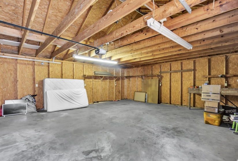 Spacious garage featuring a concrete floor, exposed wood beam ceiling, and fluorescent lighting fixtures