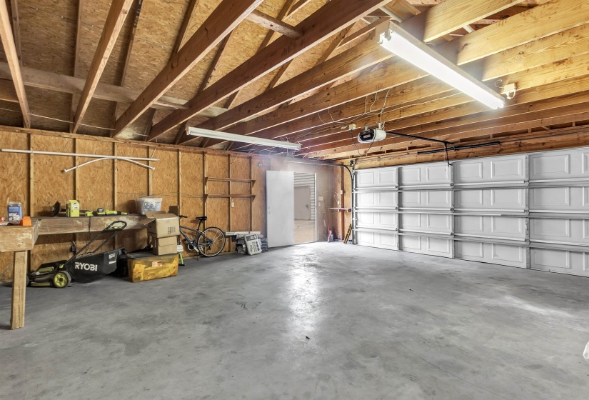 Spacious garage featuring exposed wood beam ceilings, concrete flooring, a white paneled garage door, and a built-in workbench