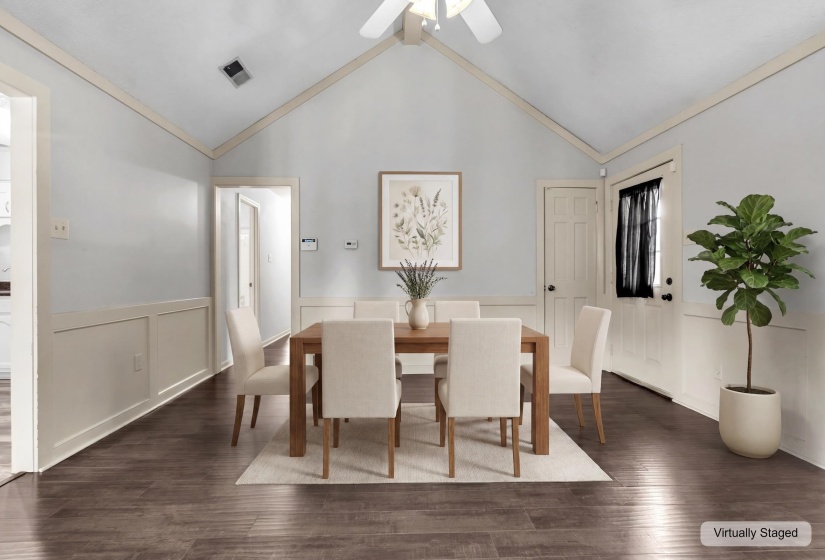 Vaulted ceiling dining area featuring wood-finish flooring, white wainscoting, and a ceiling fan with integrated lighting