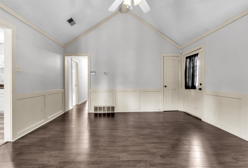 Spacious room featuring vaulted ceilings, wood-finish flooring, wainscoting, and a ceiling fan