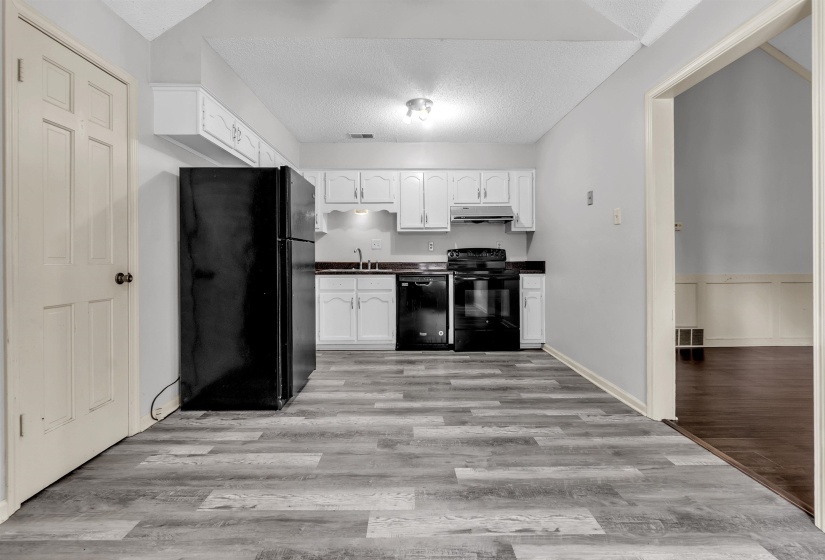 Kitchen featuring wood-finish flooring, white cabinetry, black appliances, and dark countertops