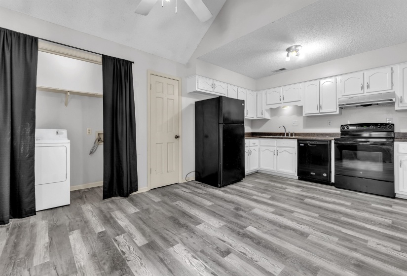 Kitchen area featuring wood-finish flooring, white cabinetry, dark countertops, and black appliances