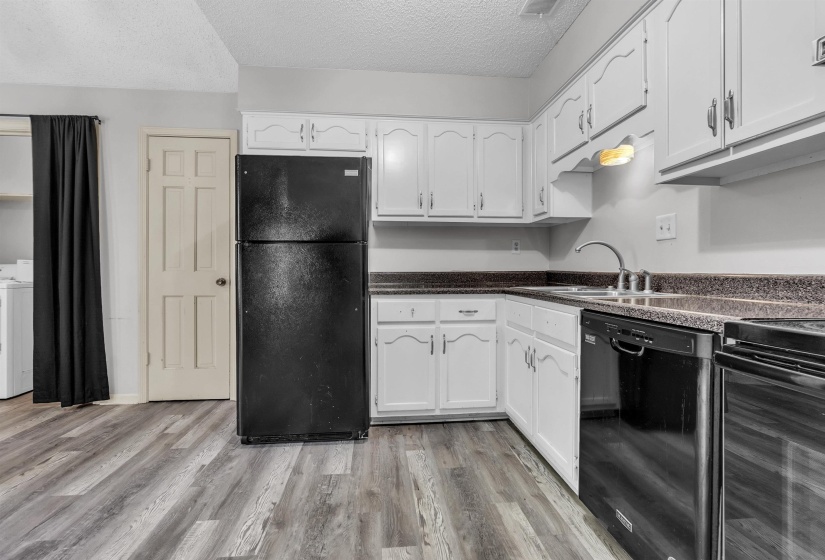 Kitchen featuring white cabinetry, dark countertops, a stainless steel sink, and wood-finish flooring