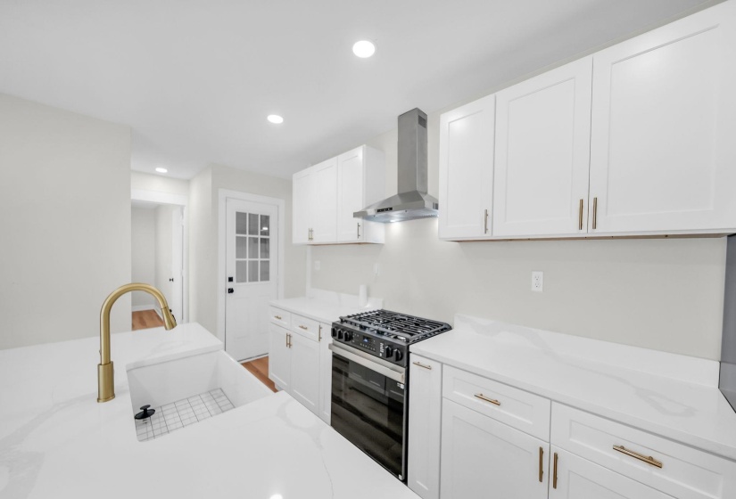 Kitchen featuring gas range oven, wall chimney exhaust hood, white cabinets, recessed lighting, and light stone countertops
