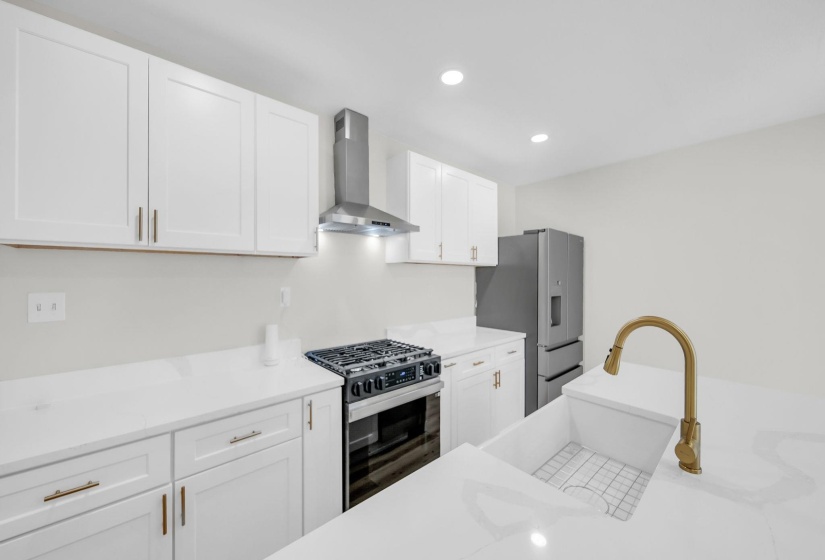 Kitchen with recessed lighting, white cabinets, gas range, wall chimney exhaust hood, and stainless steel refrigerator with ice dispenser