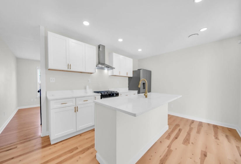 Kitchen with white cabinetry, wall chimney range hood, a center island with sink, stainless steel fridge with ice dispenser, and recessed lighting