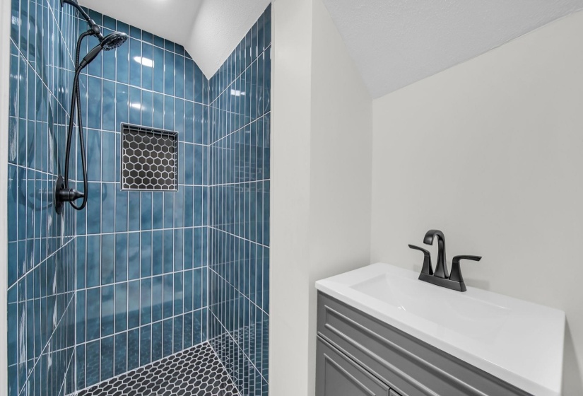 Full bathroom featuring a tile shower, vanity, and vaulted ceiling