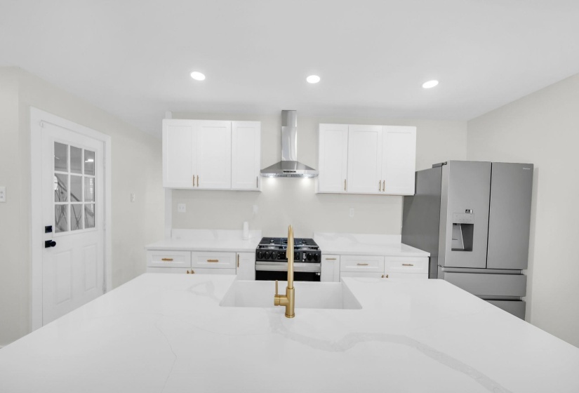 Kitchen featuring stainless steel fridge, recessed lighting, white cabinets, wall chimney range hood, and light stone counters