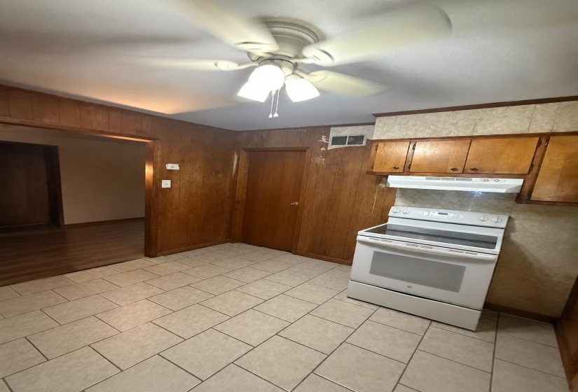 Kitchen space featuring tile flooring, wood paneling, a white electric range, wood cabinetry, and a ceiling fan with integrated lighting