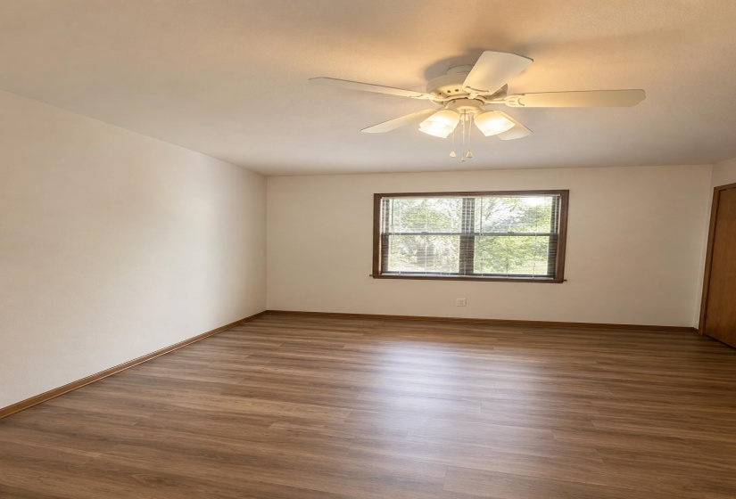 Interior room featuring wood-finish flooring, a ceiling fan with integrated lighting, and a window with wood trim