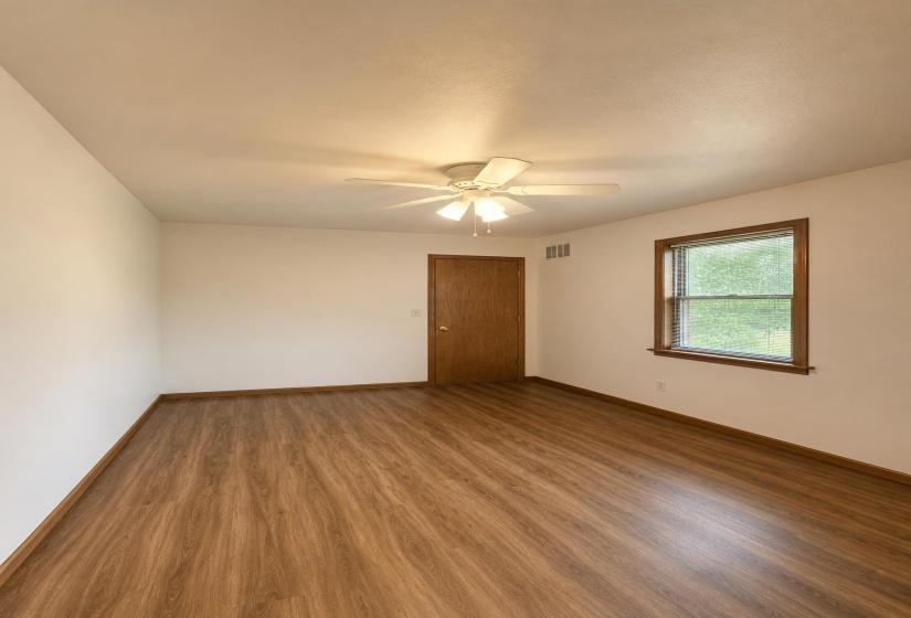 Room featuring wood-finish flooring, a white ceiling fan with integrated lighting, white walls, and a window with wood trim