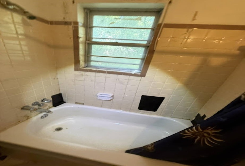 Bathtub area featuring a single-pane window, white tiled walls, a soap dish, and a wall-mounted showerhead