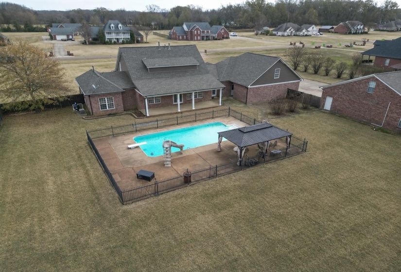 Expansive backyard featuring a fenced-in swimming pool, diving board, and slide, complemented by a covered outdoor seating area