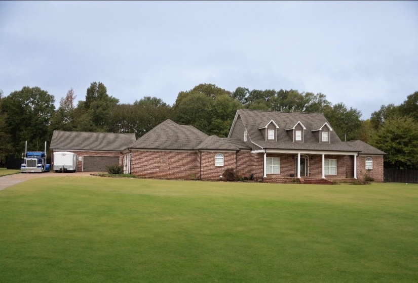 Traditional brick residence featuring a prominent gabled roofline, a front porch with white columns, and multiple dormer windows