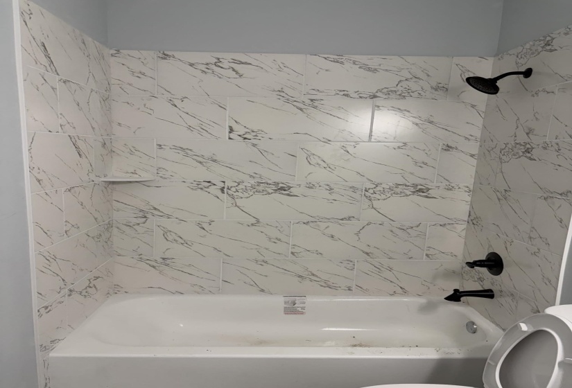 White subway tile bath surround with gray veining, black matte shower fixtures, and integrated corner shelf