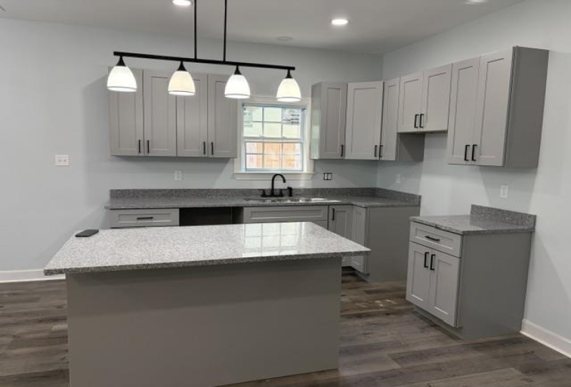 Modern kitchen featuring light gray shaker cabinetry with matte black hardware, granite-look countertops, and wood-finish flooring