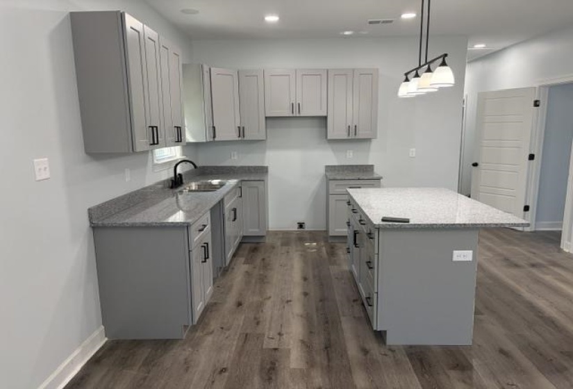 Kitchen featuring an island, light gray shaker cabinetry, stone countertops, wood-finish flooring, and a contemporary linear pendant light fixture