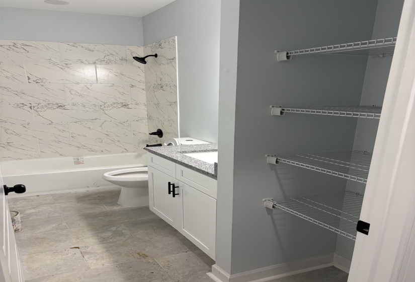 Full bathroom featuring a white tub with marble-look tile surround, a white vanity with a granite-look countertop and integral sink, and matte black fixtures