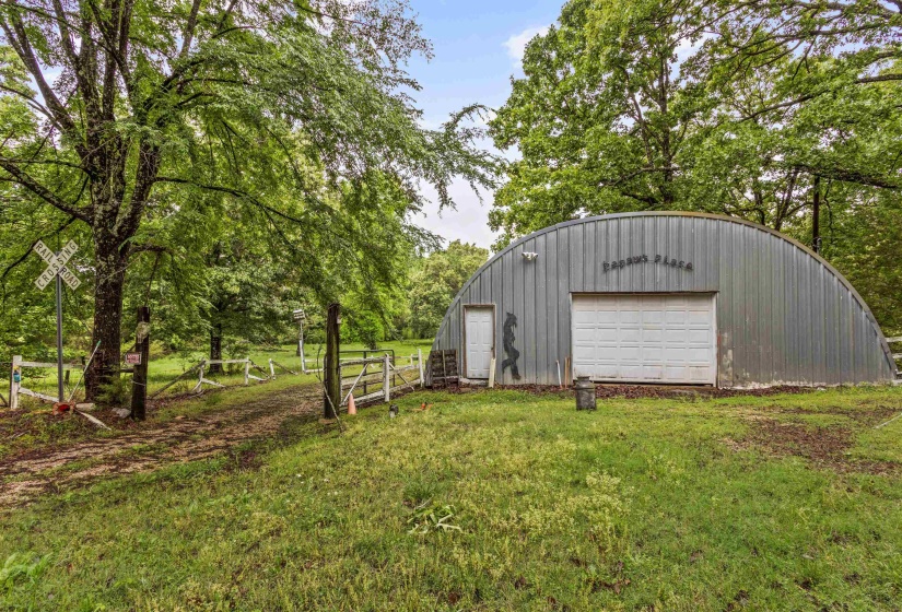 Quonset hut structure with a corrugated metal exterior, featuring a white overhead garage door and a separate entry door