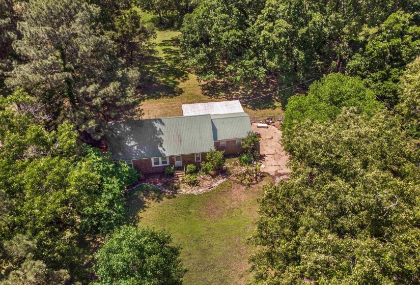 Brick residence featuring a green metal roof, a covered entry, and surrounding mature trees