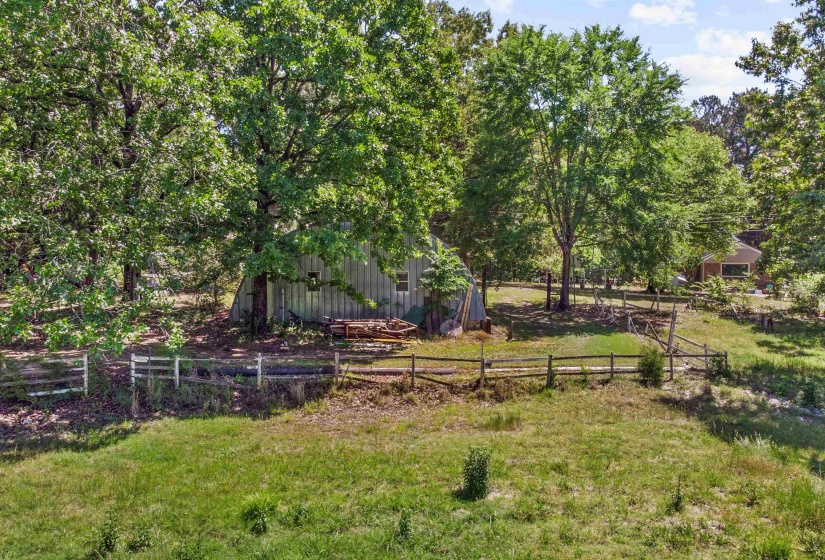 Expansive outdoor area featuring mature trees, a metal-sided outbuilding, and natural wood fencing