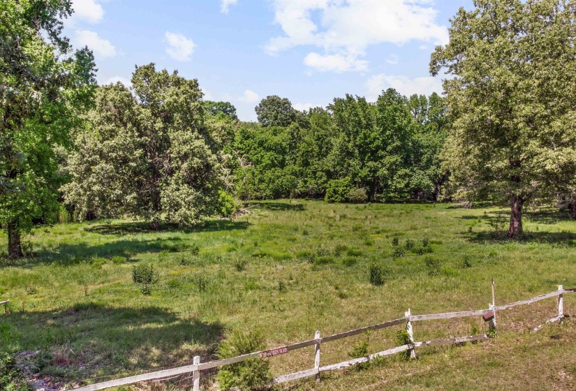Expansive open field with scattered mature trees and a partial rustic wooden fence