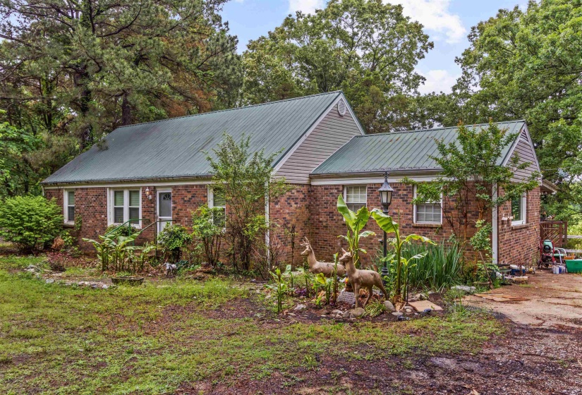 Brick residence featuring a green metal roof, partial vinyl siding, and established perimeter trees