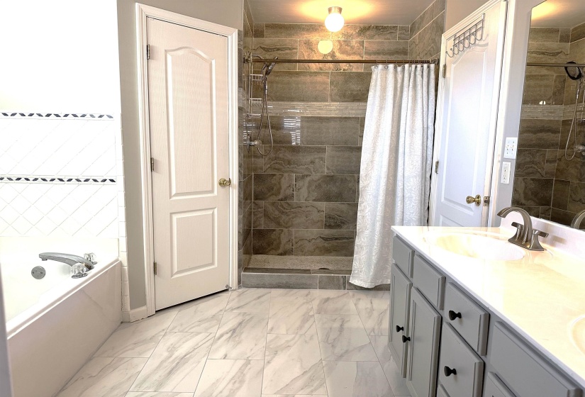 Bathroom featuring double vanity, a shower stall, a garden tub, and light marble finish floors