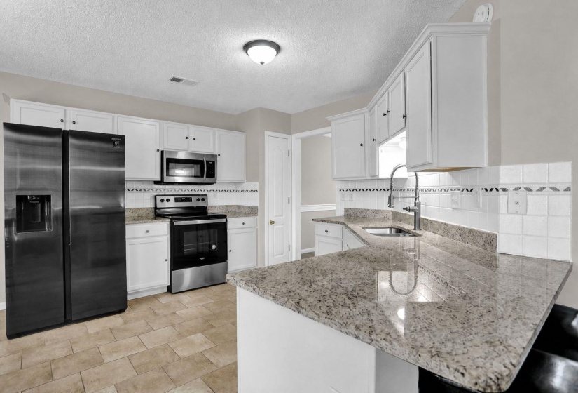 Kitchen featuring appliances with stainless steel finishes, white cabinetry, light stone countertops, and a textured ceiling