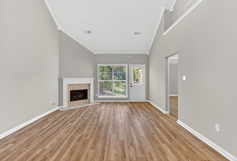 Open-concept living area featuring vaulted ceilings, wood-finish flooring, a corner fireplace with a mantel, and French doors leading to exterior