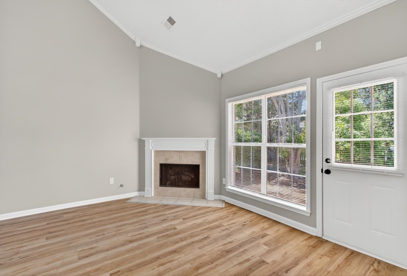 Vaulted ceiling living space featuring a fireplace with a light-colored mantel, wood-finish flooring, and large windows with blinds