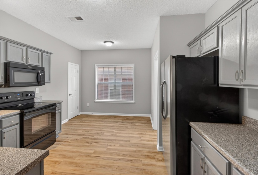 Kitchen and dining area featuring wood-finish flooring, gray cabinetry, dark countertops, and stainless steel appliances