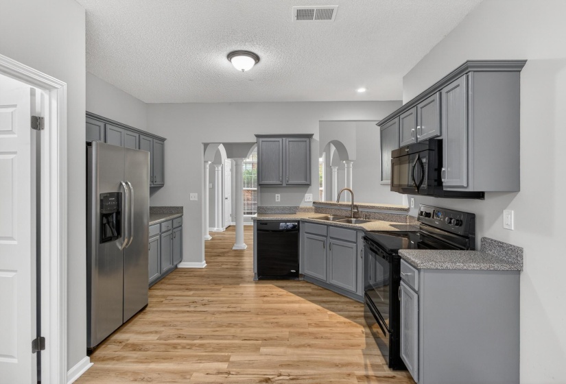Kitchen featuring grey cabinetry, stainless steel refrigerator, black stove, black microwave, and wood-finish flooring