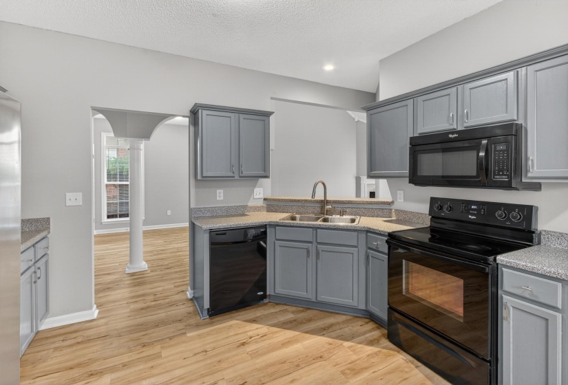 Kitchen featuring wood-finish flooring, gray cabinetry, granite-style countertops, a stainless steel sink with a gooseneck faucet, and black appliances including a range, dishwasher, and microwave