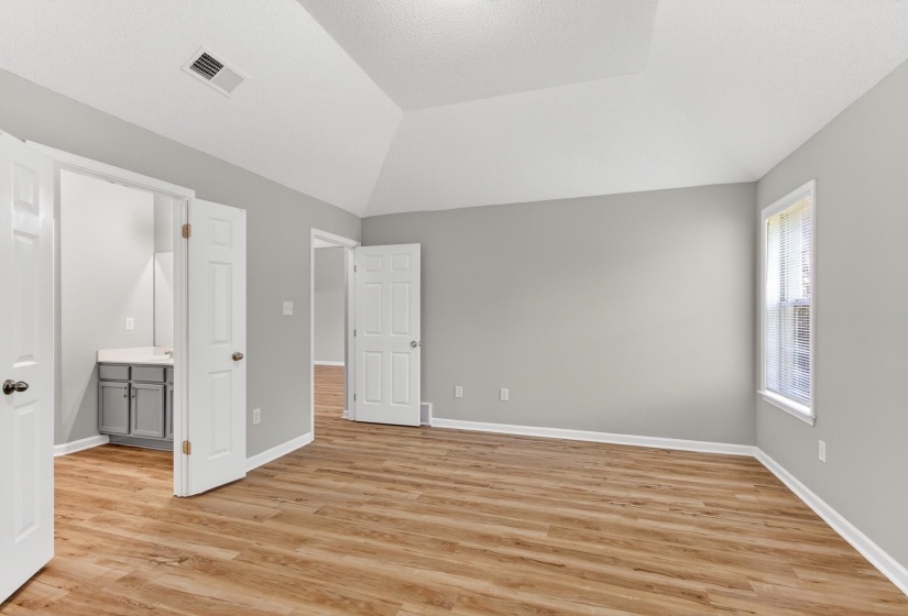 Room featuring vaulted ceilings, wood-finish flooring, light gray wall paint, and white trim