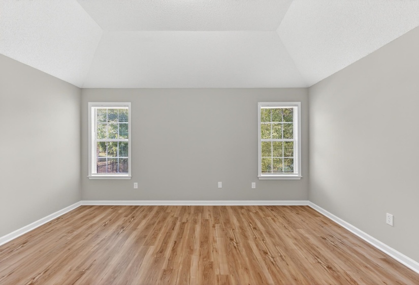 Vaulted ceiling room featuring two sash windows, wood-finish flooring, and light gray painted walls with white trim