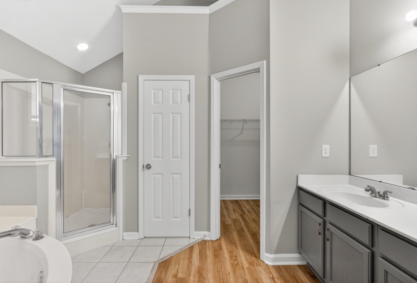 Bathroom featuring a glass-enclosed shower, a built-in soaking tub, a vanity with dual sinks and white countertops, and wood-finish flooring