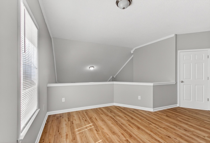 Loft area featuring wood-finish flooring, light grey painted walls, white trim, and a window with blinds
