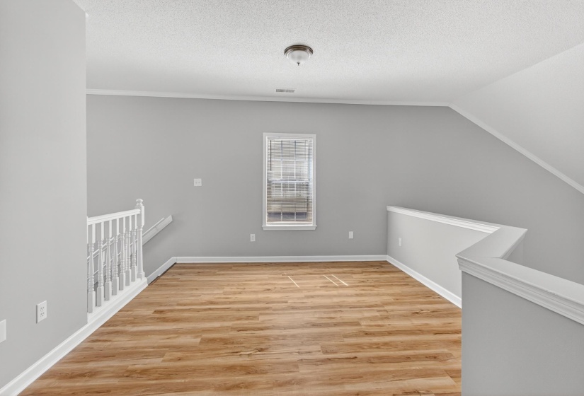 Spacious loft area featuring wood-finish flooring, light gray wall paint, a double-hung window, and white trim