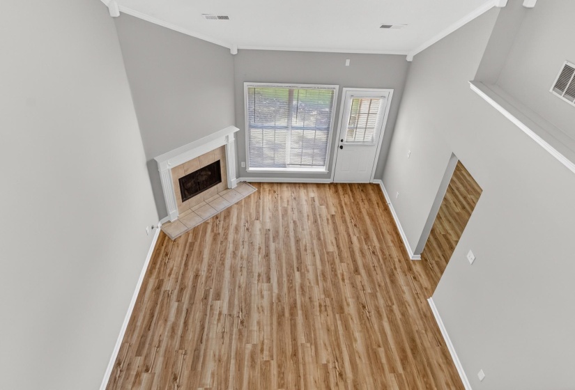 Vaulted ceiling living space featuring wood-finish flooring, a white mantel fireplace with tile hearth, and abundant natural light from a window and glass-paned door