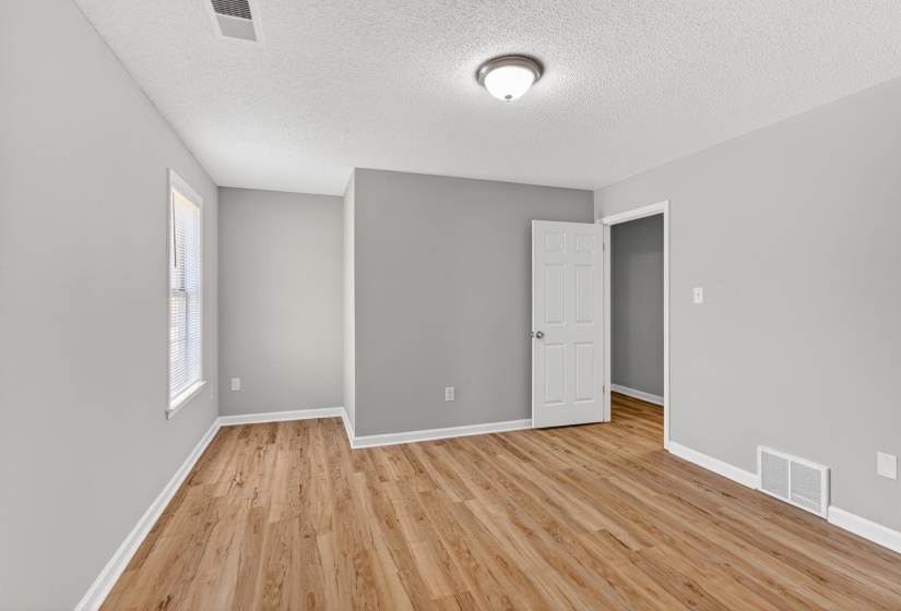 Room featuring wood-finish flooring, light gray walls, white trim, and a white six-panel interior door