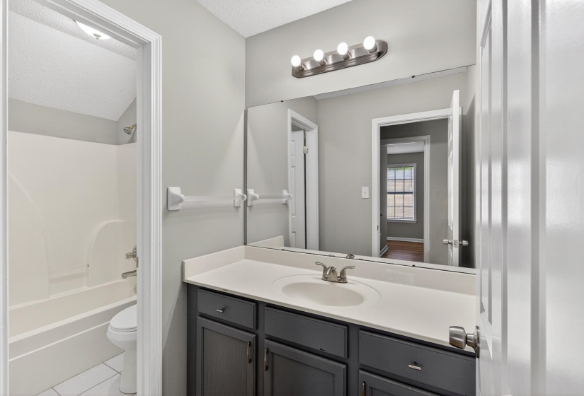 Bathroom featuring a dark vanity with a white countertop, large wall-mounted mirror, and a built-in shower/tub combination with a showerhead