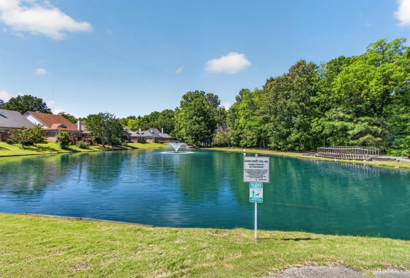 Expansive pond with a central fountain, bordered by mature trees and residential properties