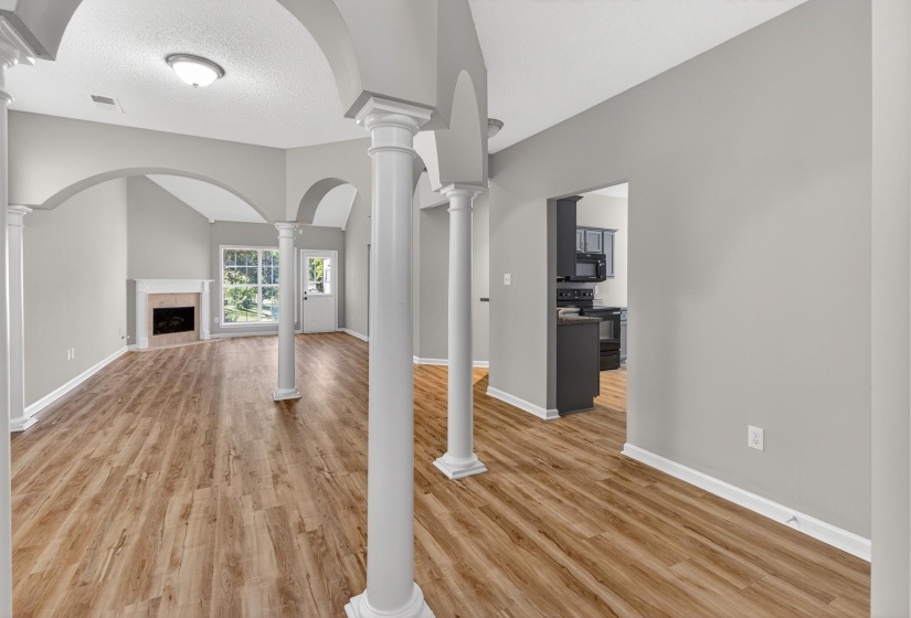 Open-concept interior featuring wood-finish flooring, vaulted ceilings, and a corner fireplace with a mantel